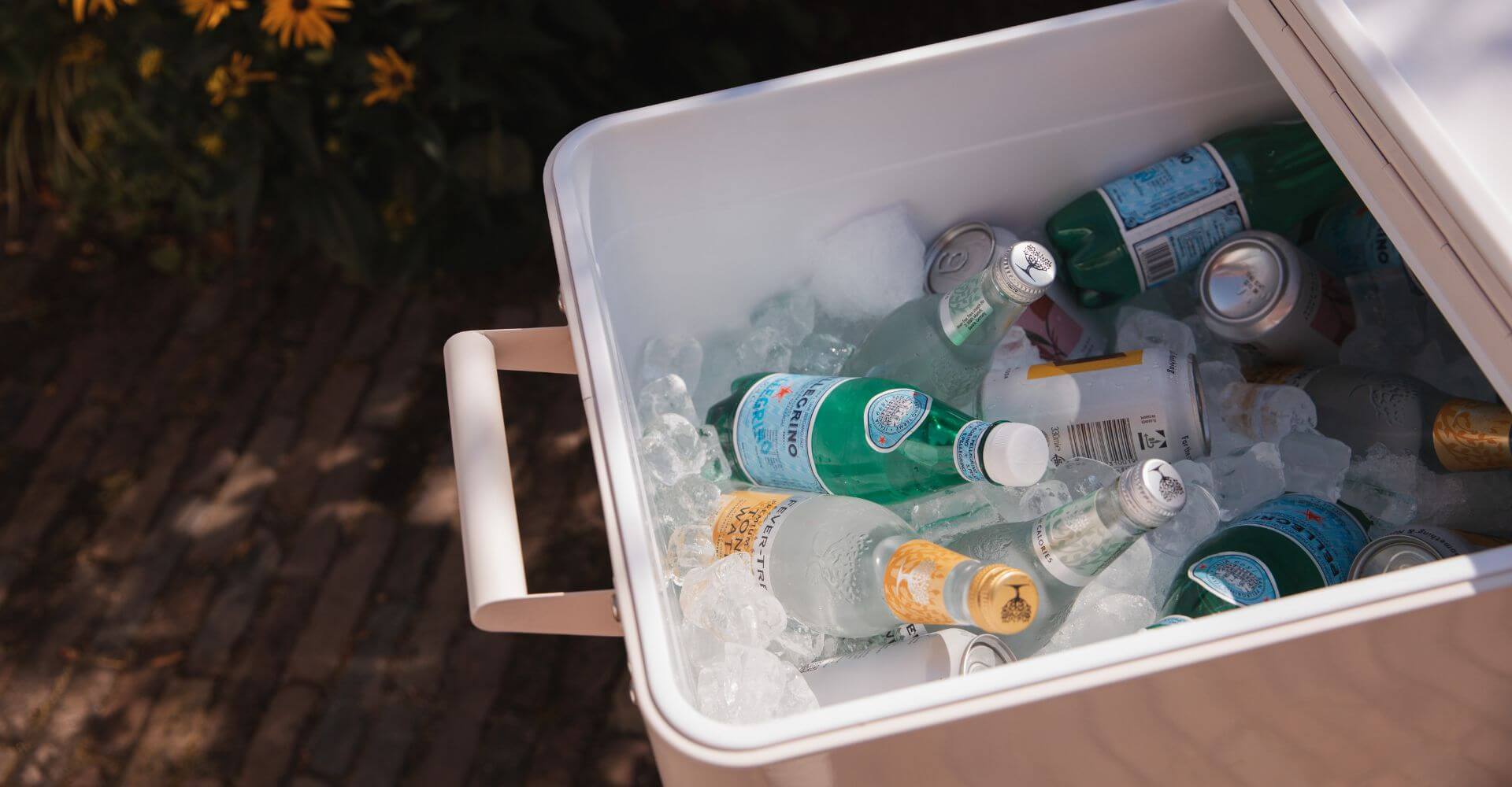 home 1 glacière design en métal crème sur une terrasse avec piscine, remplie de boissons fraîches pour profiter pleinement de l'été en extérieur.